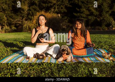Due donne si dedicano alla meditazione del bagno sonoro all'aperto in nuova Zelanda durante l'autunno. Si siedono su una coperta a righe, circondati da lussureggiante vegetazione e ser Foto Stock