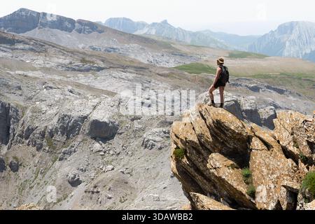 Una donna cammina lungo l'aspro terreno della Mesa de los Tres Reyes nei Pirenei, mostrando le viste panoramiche mozzafiato e l'avventuroso spir Foto Stock