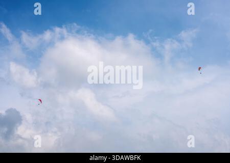 Due parapendio scivolano graziosamente nei vasti cieli blu sopra la Turchia. Le soffici nuvole bianche formano uno sfondo incredibile per questa emozionante avventura Foto Stock