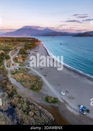 Vista aerea panoramica di Karaot Beach al tramonto, che mostra la tranquilla costa e i camper sparsi lungo la spiaggia sabbiosa, sullo sfondo di S. Foto Stock