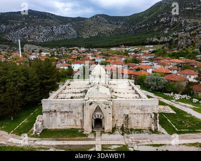 Vista aerea del Suruz Caravanserai, una splendida sistemazione medievale in Turchia, circondata da pittoresche case di villaggio dal tetto rosso e maestose montagne Foto Stock