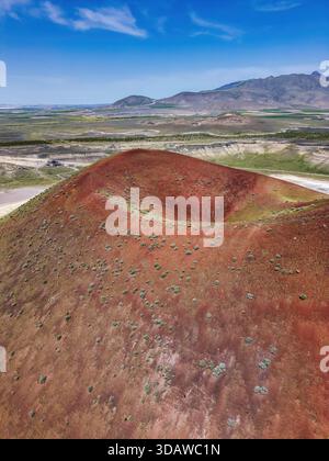 Vista aerea dello splendido lago del cratere Meke con vibrante suolo rosso e campi verdi circostanti. Il cielo azzurro e le montagne lontane creano un bordino Foto Stock