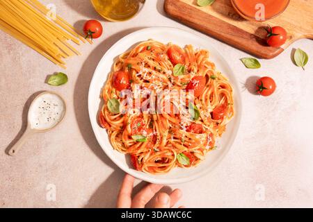 Vista dall'alto irriconoscibile della mano di una persona con un delizioso piatto di pasta condito con salsa di pomodoro fresco e parmigiano grattugiato. La piastra è posizionata a. Foto Stock