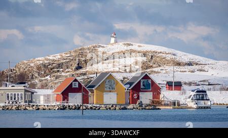 Una tranquilla vista di case colorate e un faro in cima alle colline innevate di Sommaroy, sulla costa norvegese, catturando l'essenza della pacifica Scandina Foto Stock