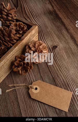 Un affascinante arredo rustico caratterizzato da pineconi naturali in una scatola di legno vintage su un tavolo in legno testurizzato, con un tag vuoto per la personalizzazione di Foto Stock