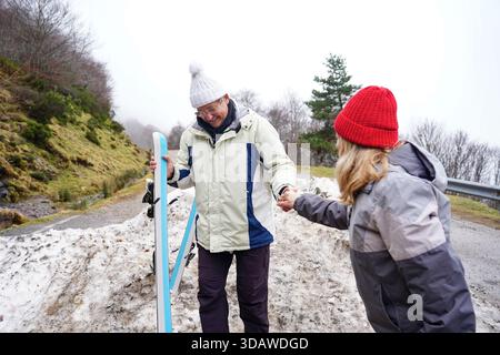 Una coppia più anziana ama praticare attività invernali in un paesaggio innevato. Indossati con calore con cappotti e cappelli, irradiano gioia e compagnia mentre abbracciano Foto Stock