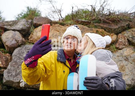 Una coppia più anziana gode di una deliziosa giornata invernale all'aperto, vestita calorosamente con cappelli e guanti. La scena cattura le loro espressioni gioiose mentre si divertono Foto Stock