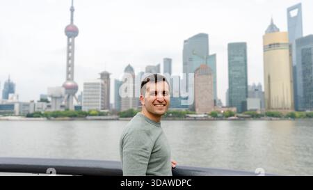 Un uomo sorride davanti a un fiume a Shanghai, in Cina, con l'iconico skyline della città, tra cui l'Oriental Pearl Tower, visibile sullo sfondo Foto Stock