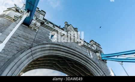 Una vista ravvicinata dell'imponente arco in pietra del Tower Bridge contro un cielo blu cristallino a Londra. Un gabbiano si innalza sopra, con parte dell'iconico ponte Foto Stock