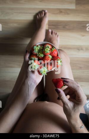 Una donna incinta regge delicatamente una ciotola di fragole fresche, simboleggiando una sana alimentazione e nutrizione. L'immagine cattura un momento sereno di connessione Foto Stock