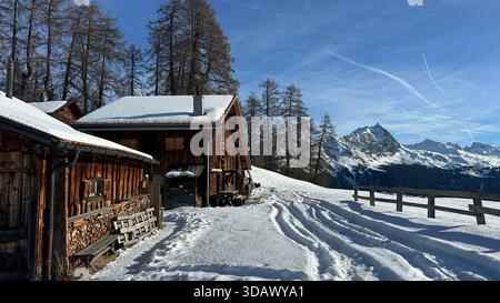 Un affascinante scenario invernale nelle Alpi svizzere a Munter vicino a Savognin Graubunden, caratterizzato da tipiche vecchie capanne alpine in legno circondate da neve bianca profonda, Foto Stock