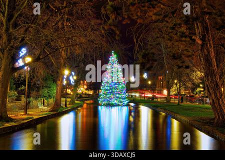 L'albero di Natale sorge nel fiume Windrush nel bellissimo villaggio Cotswolds di Bourton on the Water. Foto Stock