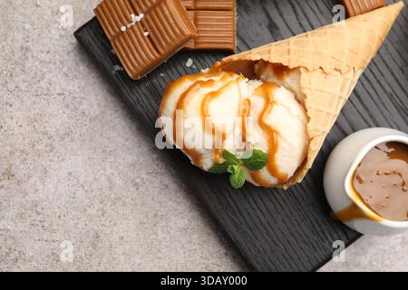 Gustoso gelato con salsa al caramello salata e menta nel cono per waffle su un tavolo grigio, piatto. Spazio per il testo Foto Stock