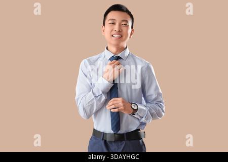 Uomo d'affari cinese che regola la cravatta su sfondo beige Foto Stock