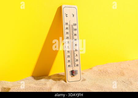 Termometro per intemperie su sabbia su sfondo giallo Foto Stock