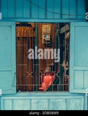 05.12.25 isola di Phu Quoc, Duong Dong. Fotografia di strada. Vista interna di una tradizionale casa vietnamita attraverso una finestra blu con griglia di sicurezza. Foto Stock