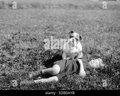Jessie Tarbox Beals - 1912-1918 - questa fotografia storica cattura un ragazzo non identificato che riposa in un campo con il suo Bulldog inglese. La foto originale è stata scattata intorno al 1912-1918 dalla pionieristica fotoreporter Jessie Tarbox Beals. L'immagine è una rappresentazione classica del legame tra un bambino e il loro animale domestico, spesso chiamata semplicemente "Un ragazzo e il suo cane" in varie ristampe. Il cane nella foto è un buon esempio della razza Bulldog di quell'epoca, prima che l'allevamento selettivo più estremo per alcuni tratti fisici diventasse comune. Foto Stock