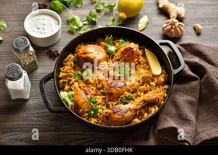 Deliziosi biriyani di pollo fatti in casa serviti in una padella di ghisa su un tavolo di legno scuro. Piatto indiano tradizionale. Vista ravvicinata Foto Stock