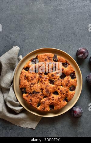 Torta di prugne autunnale calda su un piatto con sfondo in pietra blu e spazio libero. Vista dall'alto, disposizione piatta. Foto Stock