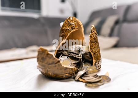 Scatola portamonete in ceramica rotta piena di monete in euro all'interno della casa. Concetto di debito delle famiglie, aumento delle spese, pressione sul bilancio, stress finanziario ed ev Foto Stock