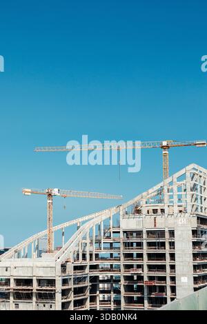 Un grande cantiere con telai in cemento parzialmente costruiti e due gru a torre che si estendono su un cielo azzurro. L'immagine cattura urbano deve Foto Stock