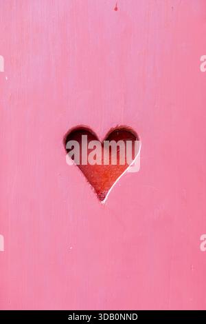 Una superficie in legno rosa brillante presenta una delicata fessura a forma di cuore che rivela un caldo interno rosso. Questa immagine trasmette amore, tenerezza e accogliente rom Foto Stock