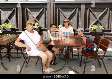 Donna, uomo, ragazzo e bambino seduti al tavolino all'aperto. Famiglia in vacanza estiva. Riunione multigenerazionale al ristorante. Foto Stock