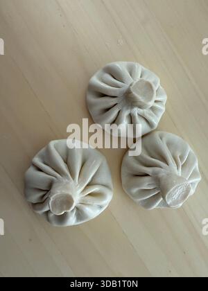 tre gnocchi di khinkali georgiano crudi su una superficie di legno chiaro, concetto di cibo fatto in casa Foto Stock