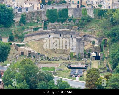 Vista sopraelevata delle rovine del Teatro Romano del i secolo a.C. a Volterra, Italia, che mostra cavea di pietra, resti di scena e mura circostanti. Foto Stock