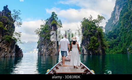 Una coppia in piedi mano nella mano lungo una tradizionale barca di legno sulle calme acque del lago Cheow LAN. Khao Sok Thailandia Foto Stock