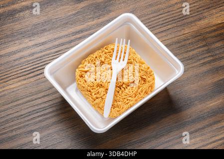 Spaghetti istantanei essiccati e forchetta monouso bianca in piastra di plastica Foto Stock