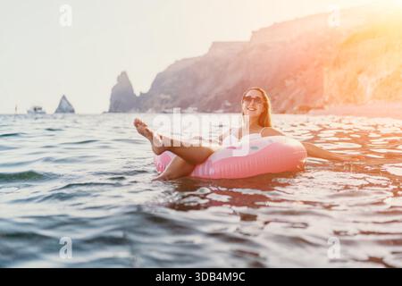 Donna, mare, relax. Una donna felice si rilassa su una ciambella gonfiabile nel mare tranquillo al tramonto, ideale per lo spazio fotocopie. Foto Stock