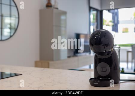 Primo piano della macchina per il caffè a capsule nere in un'elegante cucina con piano in marmo e unità TV Foto Stock