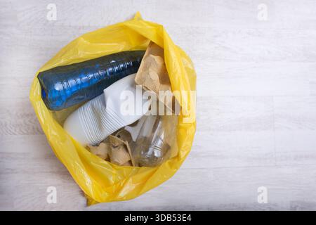 Il sacchetto giallo contiene articoli riciclabili assortiti, come bottiglie di plastica, bicchieri e cartone, che evidenziano l'importanza di uno smaltimento corretto dei rifiuti e di Foto Stock