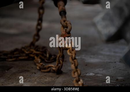 Catena per impieghi pesanti ruggine appesa e distesa sul pavimento della fabbrica catturata in profondità ridotta di sicurezza industriale sul campo e dettagli sulle attrezzature Foto Stock