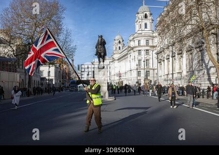 Londra, Inghilterra, Regno Unito. 13 dicembre 2025. Un manifestante inonda una bandiera Union Jack durante l'evento "Unite the Kingdom" a Whitehall. La manifestazione, organizzata dall'attivista di estrema destra Tommy Robinson, è stata inquadrata come un servizio carol per promuovere i valori britannici e l'eredità cristiana. L'evento, che ha attirato circa 1.000 partecipanti, è stato accolto con una significativa presenza della polizia e una vicina contro-protesta di Stand Up to Racism. Crediti: horst friedrichs/Alamy Live News Foto Stock