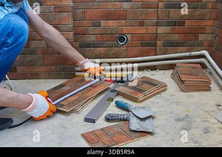 il muratore che lavora in cucina misura il metro a nastro per la lunghezza della piastrella Foto Stock