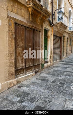 Una strada tranquilla a Malta mostra il vecchio negozio Vincent Pizzuto Upholsterer. L'architettura dell'edificio e la facciata intemprata raccontano una storia del passato, inv Foto Stock