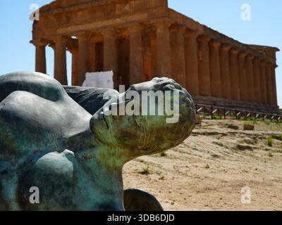 Una scultura contemporanea in bronzo dell'uomo, con un antico tempio dorico greco sullo sfondo della Valle dei Templi, Agrigento, Sicilia, Italia. Foto Stock