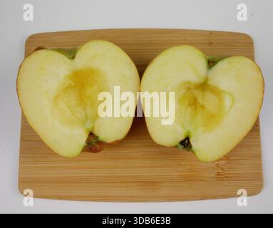 Vista dall'alto di due metà di mele fresche su un tagliere di legno su sfondo bianco, semplice ingrediente di frutta per la ricetta del dessert di mele al forno fatta in casa Foto Stock