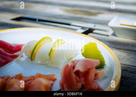 Una fotografia ravvicinata mostra i nigiri di pesce adornati con fette di lime fresche, accompagnati da zenzero sottaceto su un piatto di ceramica. Si trova su di un rustico legno Foto Stock