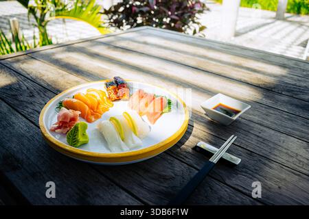 Una selezione di sushi nigiri con salmone, tonno e pesce bianco viene presentata su un piatto di ceramica con zenzero, spicchi di lime e salsa di soia. Bacchette Foto Stock