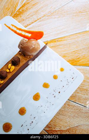 Un ricco brownie con torta al cioccolato è adornato da una paletta di gelato al cioccolato, completato da vivaci scaglie di caramello arancio e noci sparse. Foto Stock