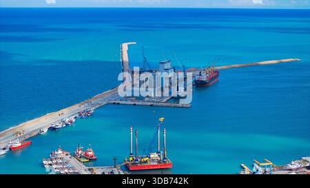Foto aeree che catturano il mare turchese di Ortona, tranquille increspature sulla costa, navi ormeggiate e servizi portuali pieni illuminati dalla luminosa S. Foto Stock