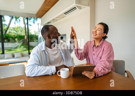 Felice coppia multietnica che utilizza un notebook, acquista online con le vendite, gioca insieme Foto Stock