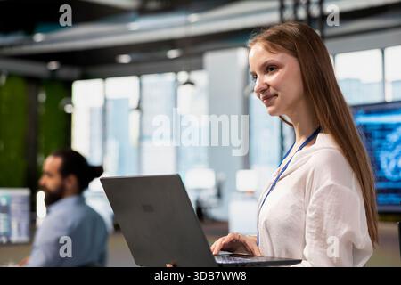 Ingegnere donna allegra che regola i parametri degli algoritmi di deep learning sul laptop per automatizzare le attività. Stagista di una società tecnologica che lavora con informazioni basate sull'intelligenza artificiale sui notebook per l'ottimizzazione del codice Foto Stock