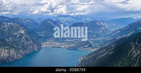 Alta vista aerea sul Lago di Garda settentrionale verso Riva del Garda, incorniciata da ripide scogliere calcaree e colline alpine boscose. Foto Stock
