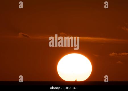 Il sole si illumina sopra le nuvole basse al tramonto, diffondendo una calda luce dorata sul cielo in un ambiente tropicale. Foto Stock
