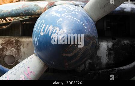 Primo piano dettagliato di un'elica di un vecchio aereo, che mostra un cono blu intemprato ricoperto di graffiti e graffi, circondato da metallo usurato Foto Stock