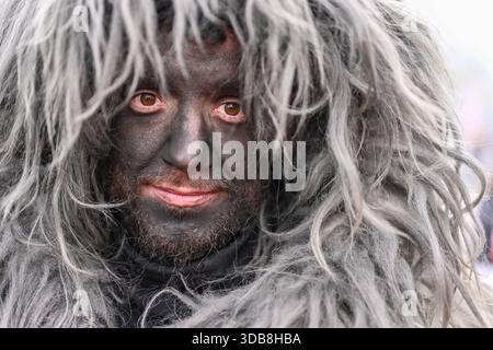 I mamutoni che indossano maschere di legno scuro, indumenti in montone e campane pesanti partecipano a una tradizionale processione di Carnevale a Mamoiada, in Sardegna, Italia. Foto Stock